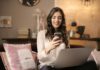7 Online Banks That Pay Early woman sitting on sofa while looking at phone with laptop on lap